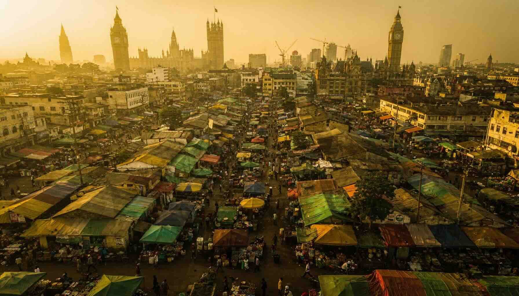 Aerial golden-hour shot of Kumasi's central market from above — dense colourful canopies, crowds, traders — with a subtle double exposure overlay of a European city skyline (London or Amsterdam) fading into the scene.